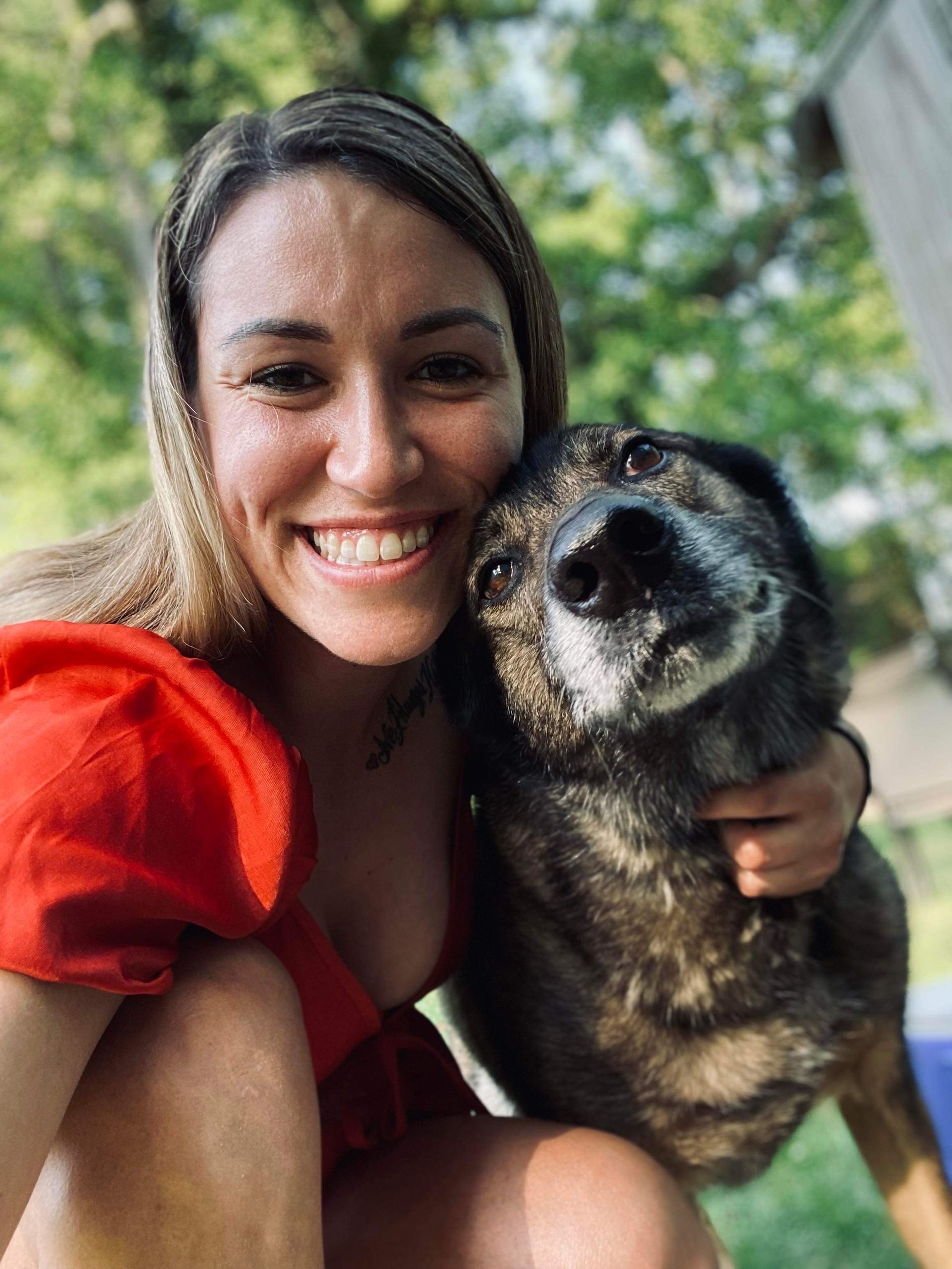 A woman is kneeling down next to a dog and smiling.
