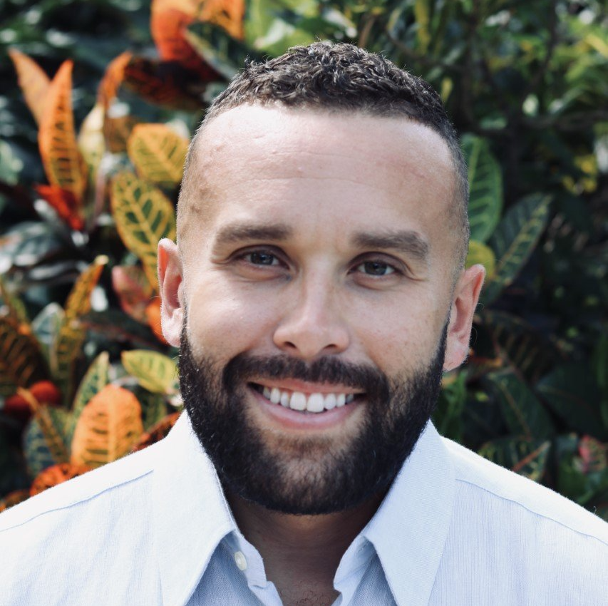 A man with a beard is smiling and wearing a white shirt