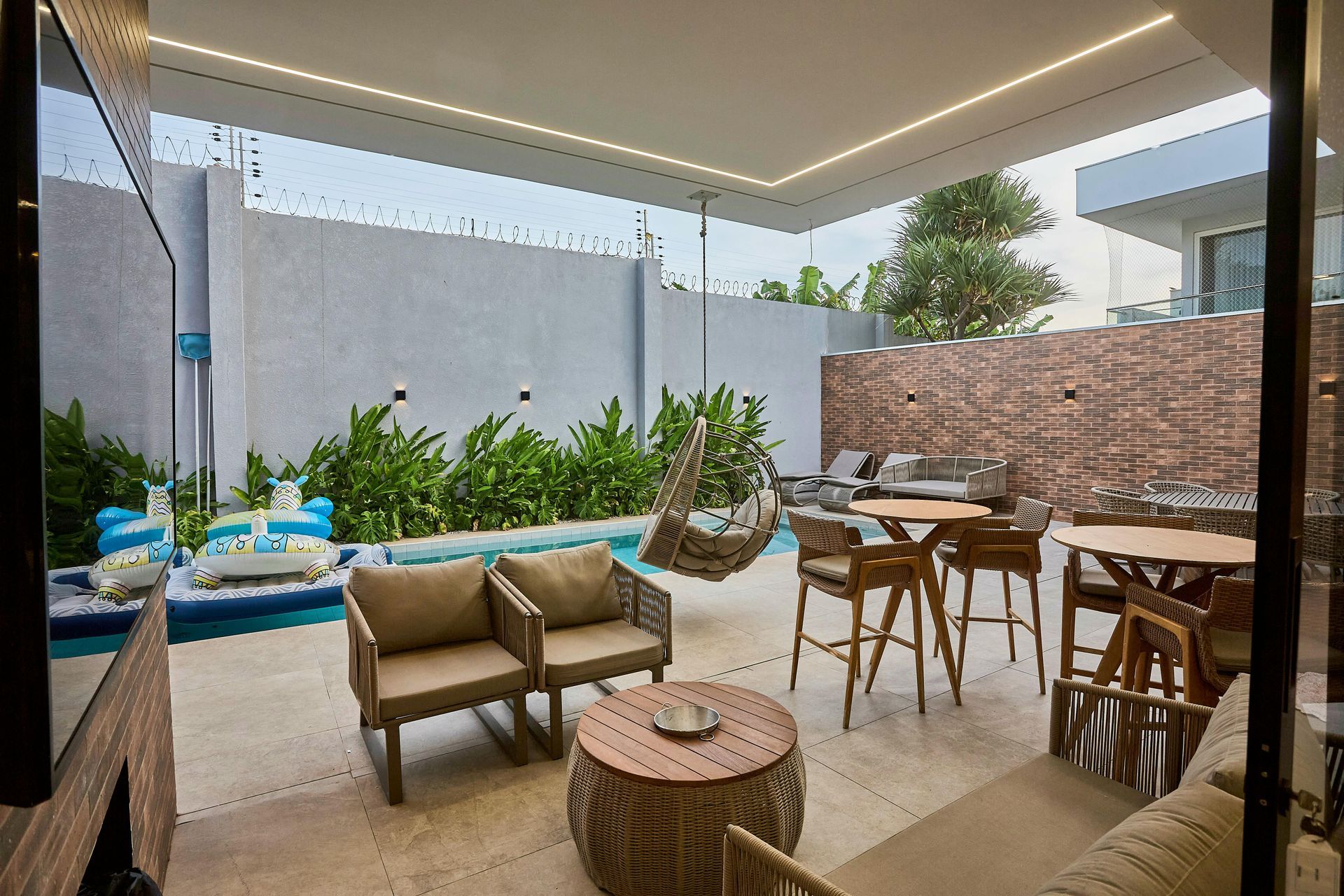 Modern covered patio with lounge chairs, dining table, plants, and an outdoor sofa by a small pool