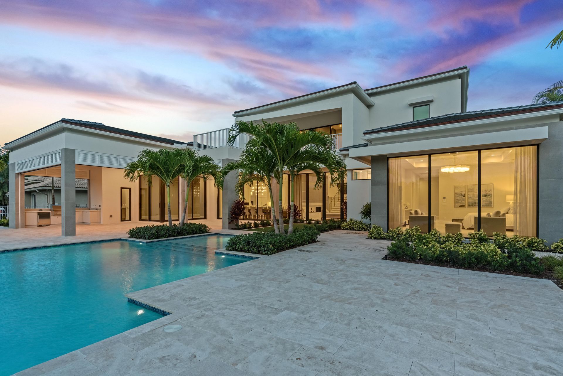 Modern luxury home with a turquoise pool and palm trees at sunset