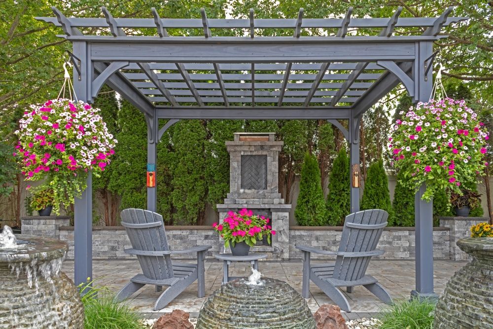 Covered garden patio with gray chairs, hanging pink flowers, and a stone fountain backdrop