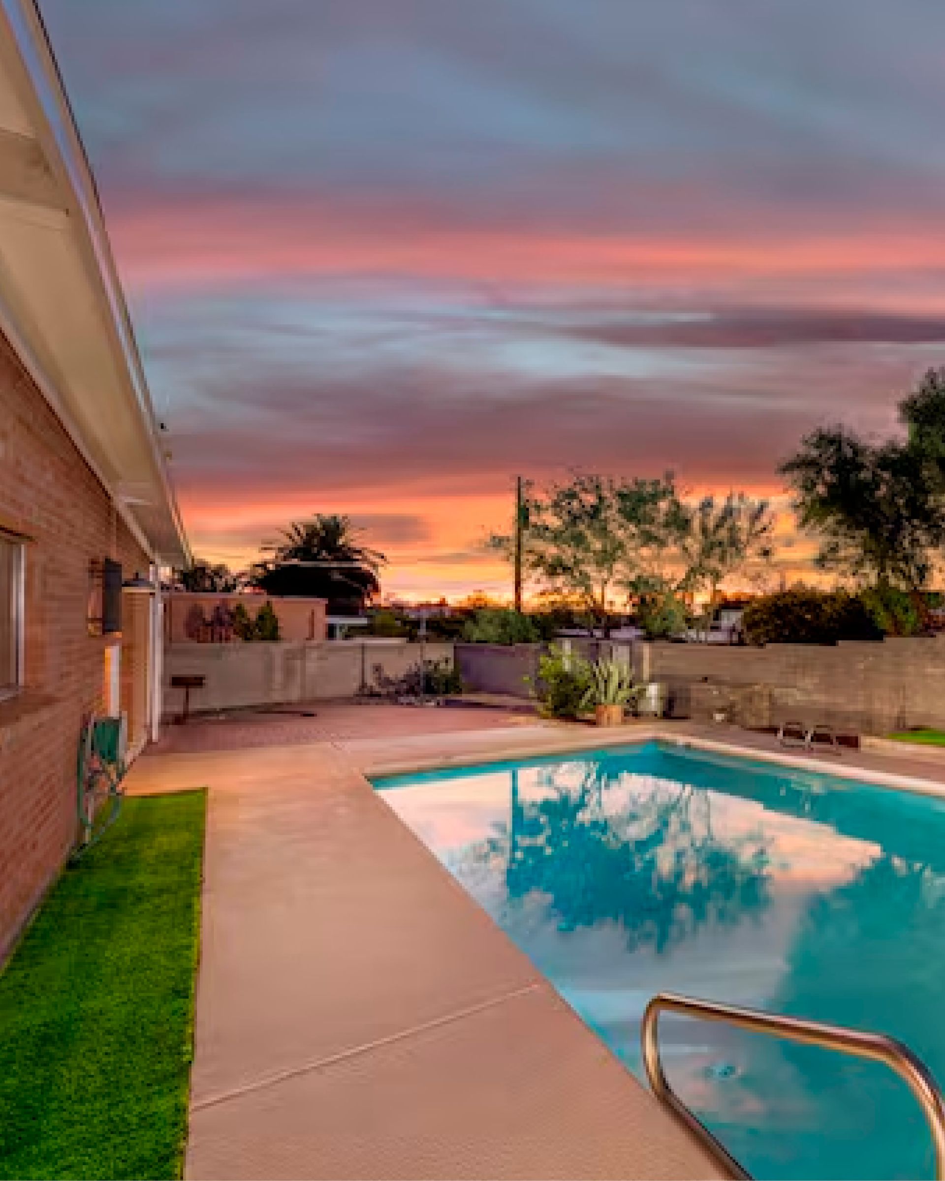 Backyard pool at sunset with pink sky, patio, and house exterior reflected in the water