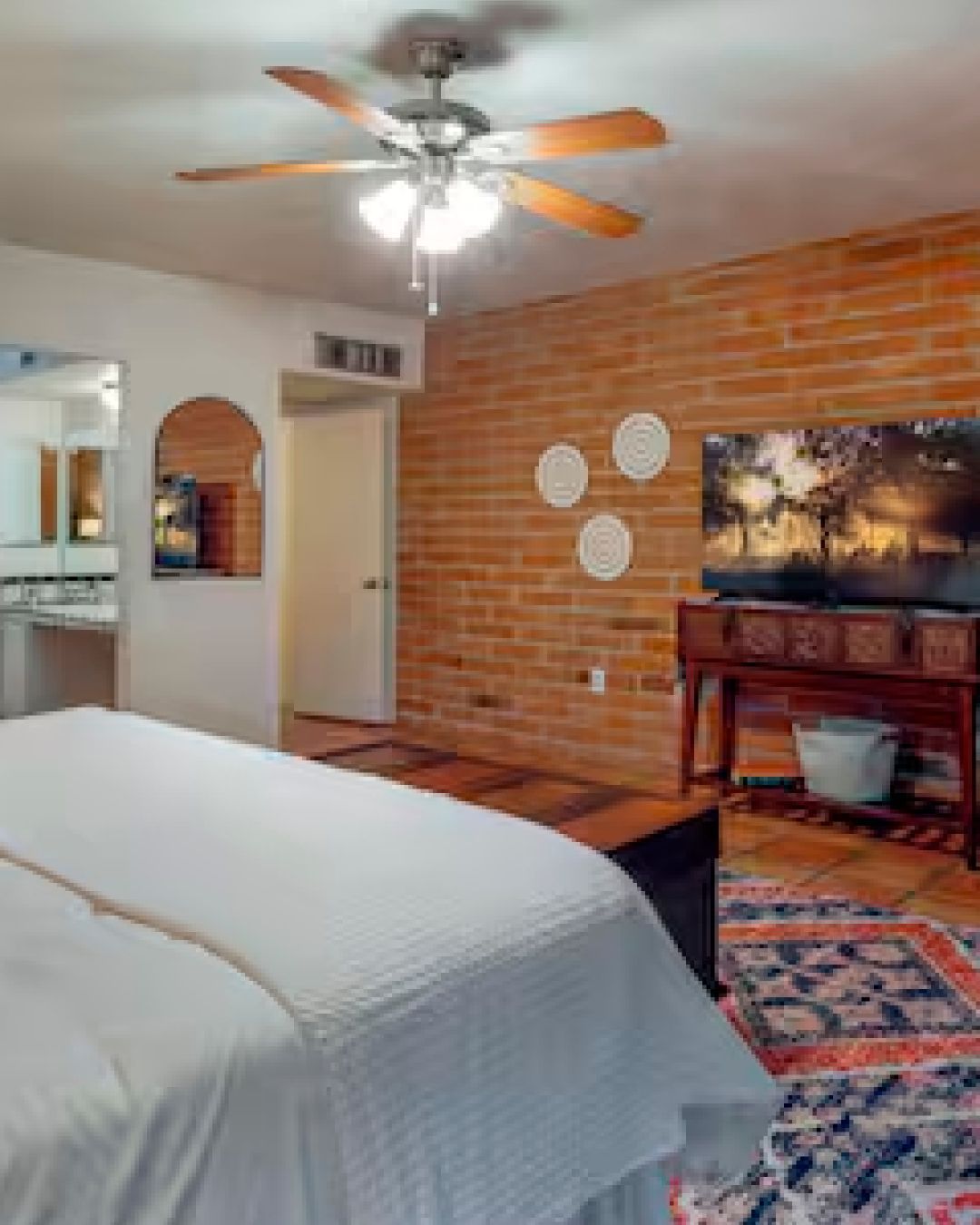 Cozy bedroom with brick accent wall, ceiling fan, bed, and patterned rug