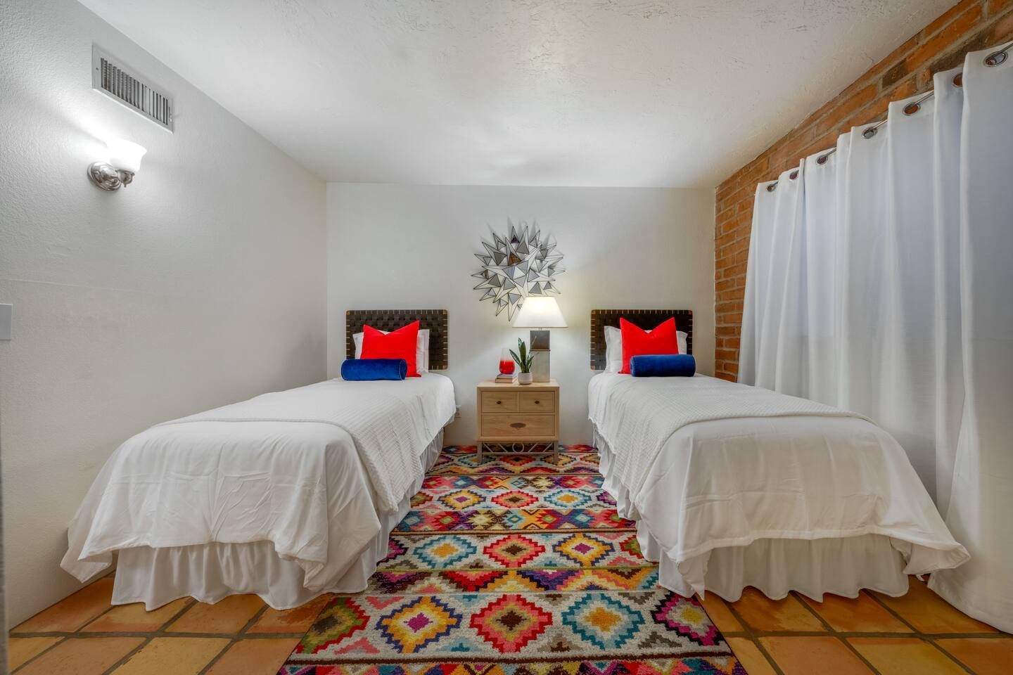 Twin beds in a bright bedroom with colorful rug and a nightstand between them
