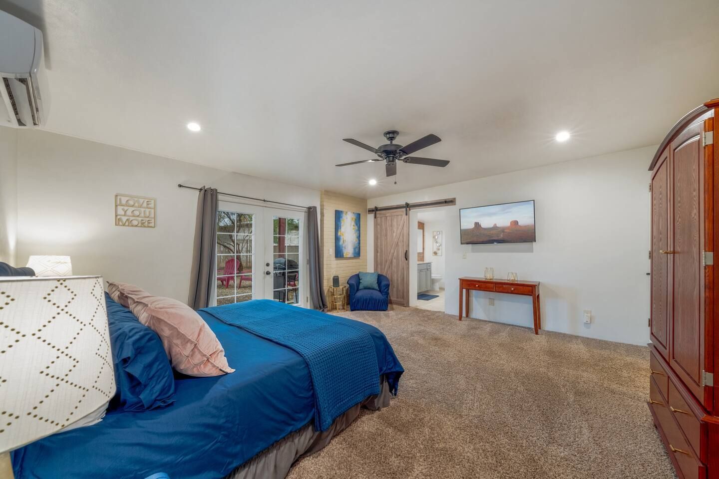 Spacious bedroom with blue bedspread, carpet, ceiling fan, and wooden armoire, viewed from the doorway