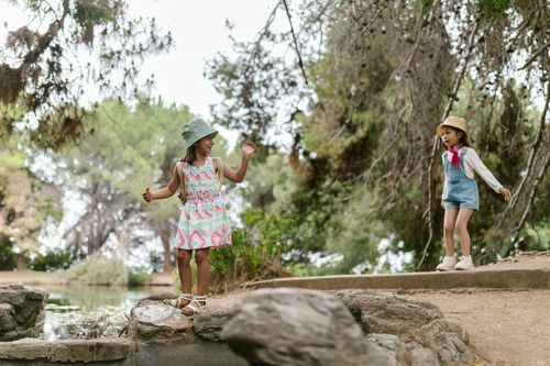 Two children in sun hats explore a wooded creekside path outdoors