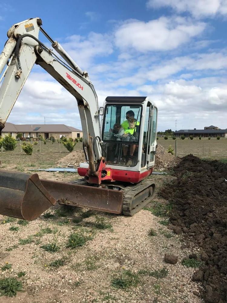 A Man Is Driving An Excavator In A Dirt Field — Justin Drew Plumbing in Grovedale, VIC