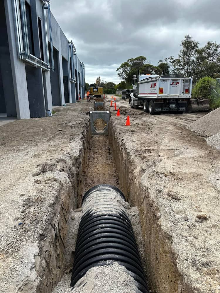 A Large Pipe Is Being Installed In The Dirt Next To A Dump Truck — Justin Drew Plumbing in Grovedale, VIC