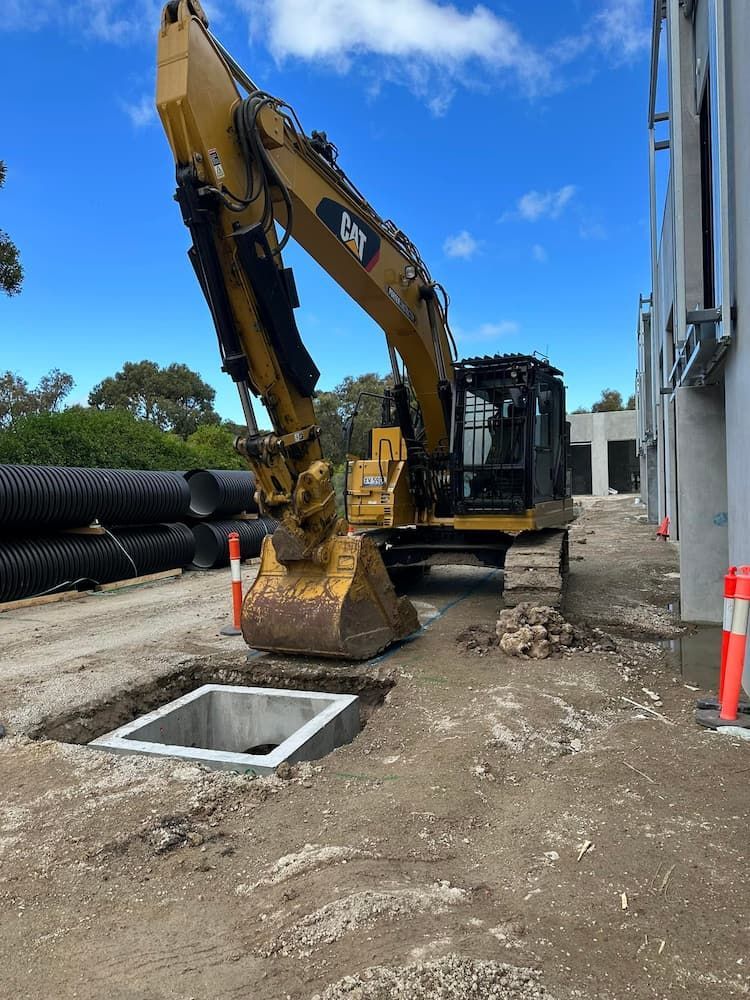 A Cat Excavator Is Digging A Hole In The Ground — Justin Drew Plumbing in Grovedale, VIC
