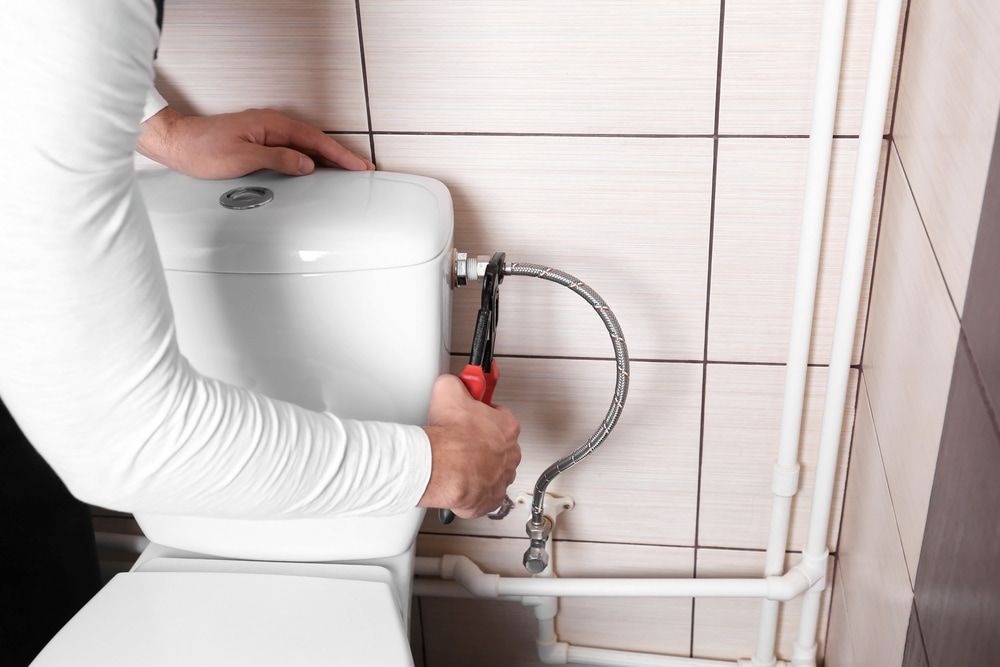A Man Is Fixing A Toilet In A Bathroom With A Wrench — Justin Drew Plumbing in Torquay, VIC