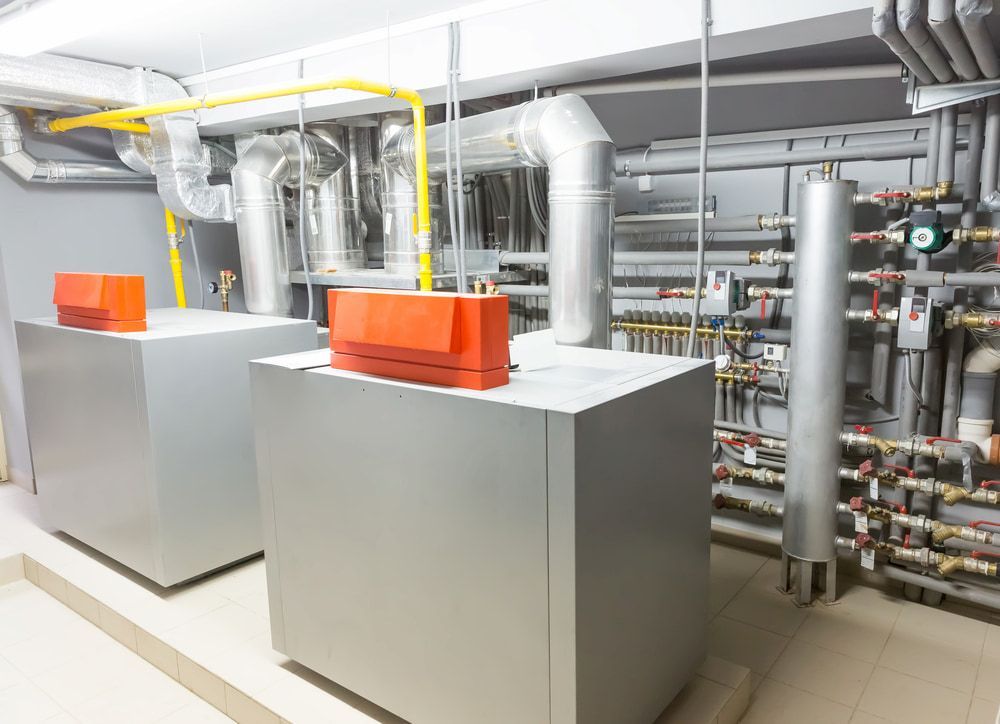 Two Boilers Are Sitting Next To Each Other In A Room With Pipes — Justin Drew Plumbing in Newtown, VIC