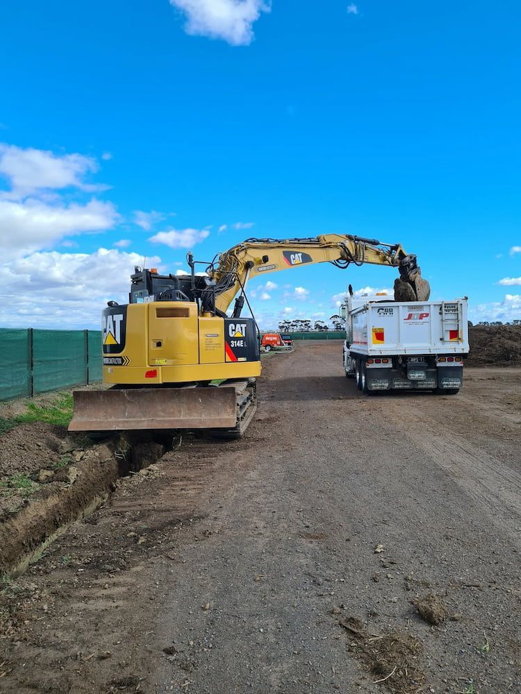 A Bulldozer Is Loading Dirt Into A Dump Truck On A Dirt Road — Justin Drew Plumbing in Torquay, VIC