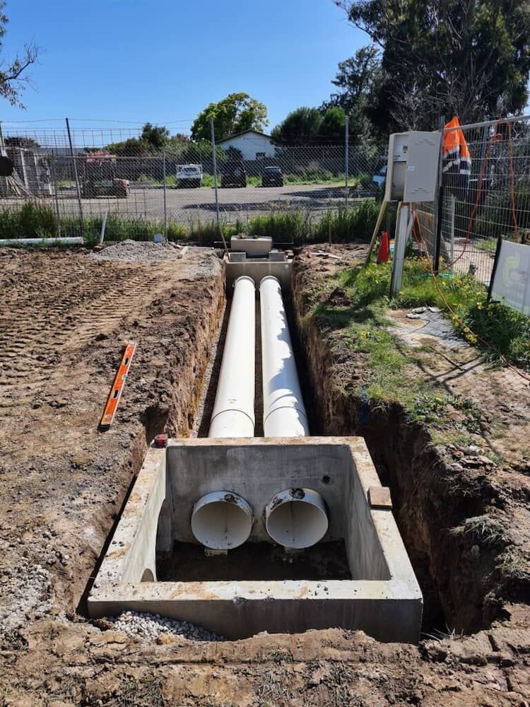 Two White Pipes Are Being Installed In A Hole In The Ground — Justin Drew Plumbing in Torquay, VIC