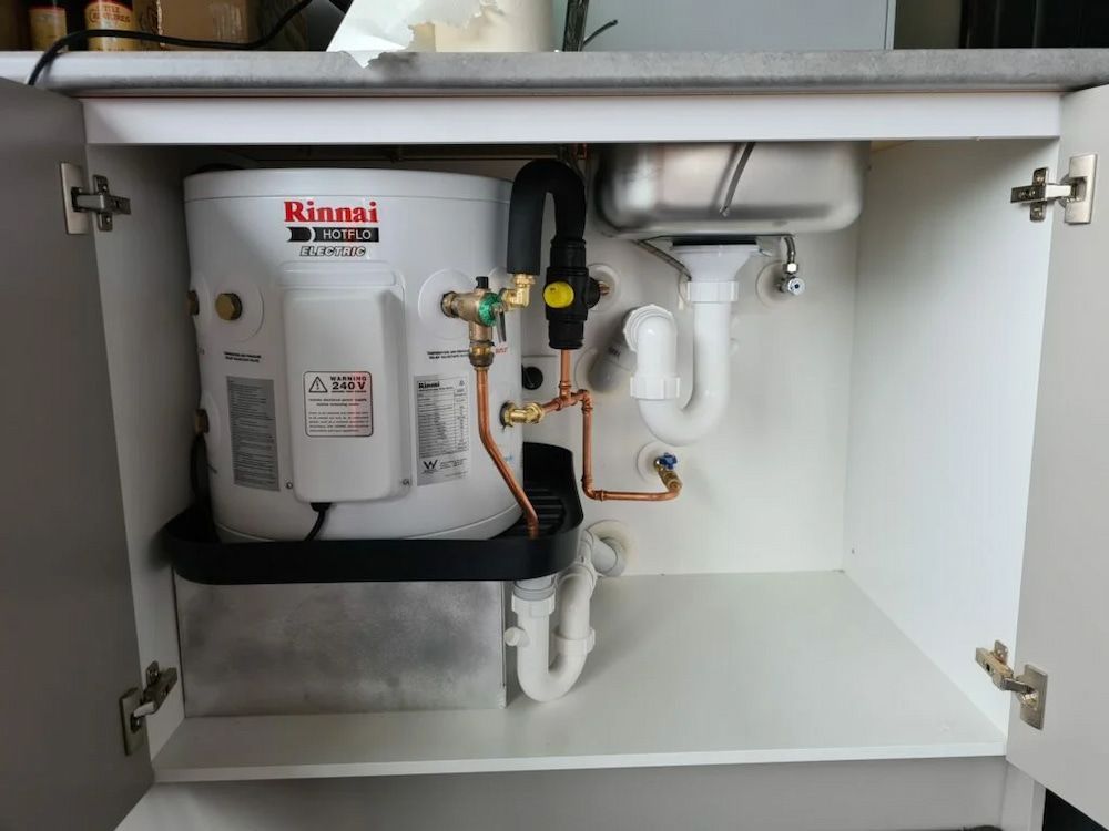 A Water Heater Is Sitting Under A Sink In A Cabinet — Justin Drew Plumbing in Torquay, VIC