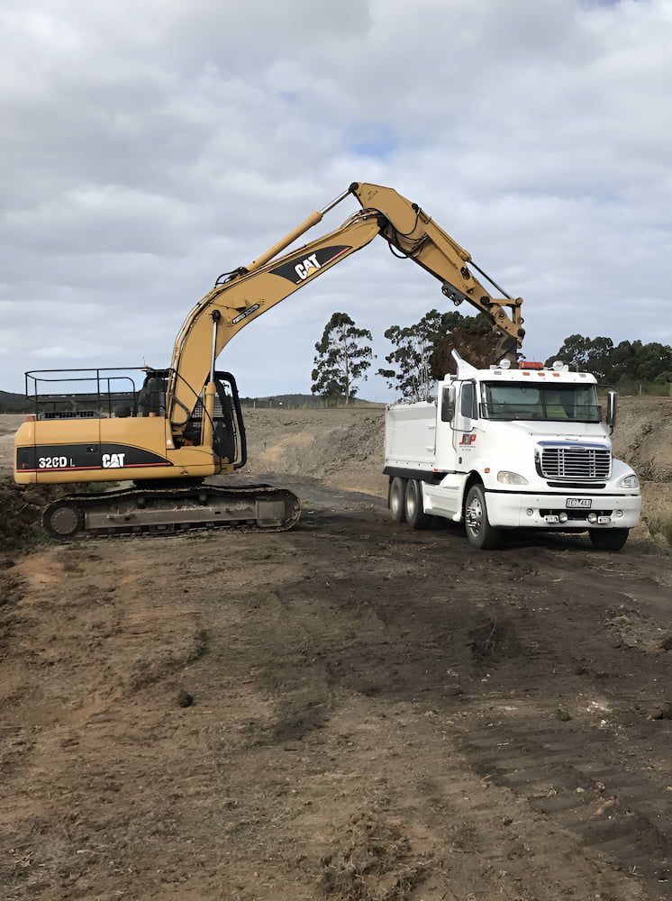 An Excavator Is Loading Dirt Into A Truck On A Dirt Road — Justin Drew Plumbing in Grovedale, VIC