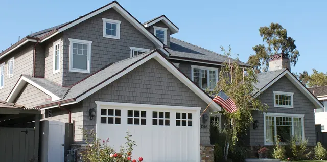 Gray suburban house with white garage and windows, American flag, and landscaped front yard