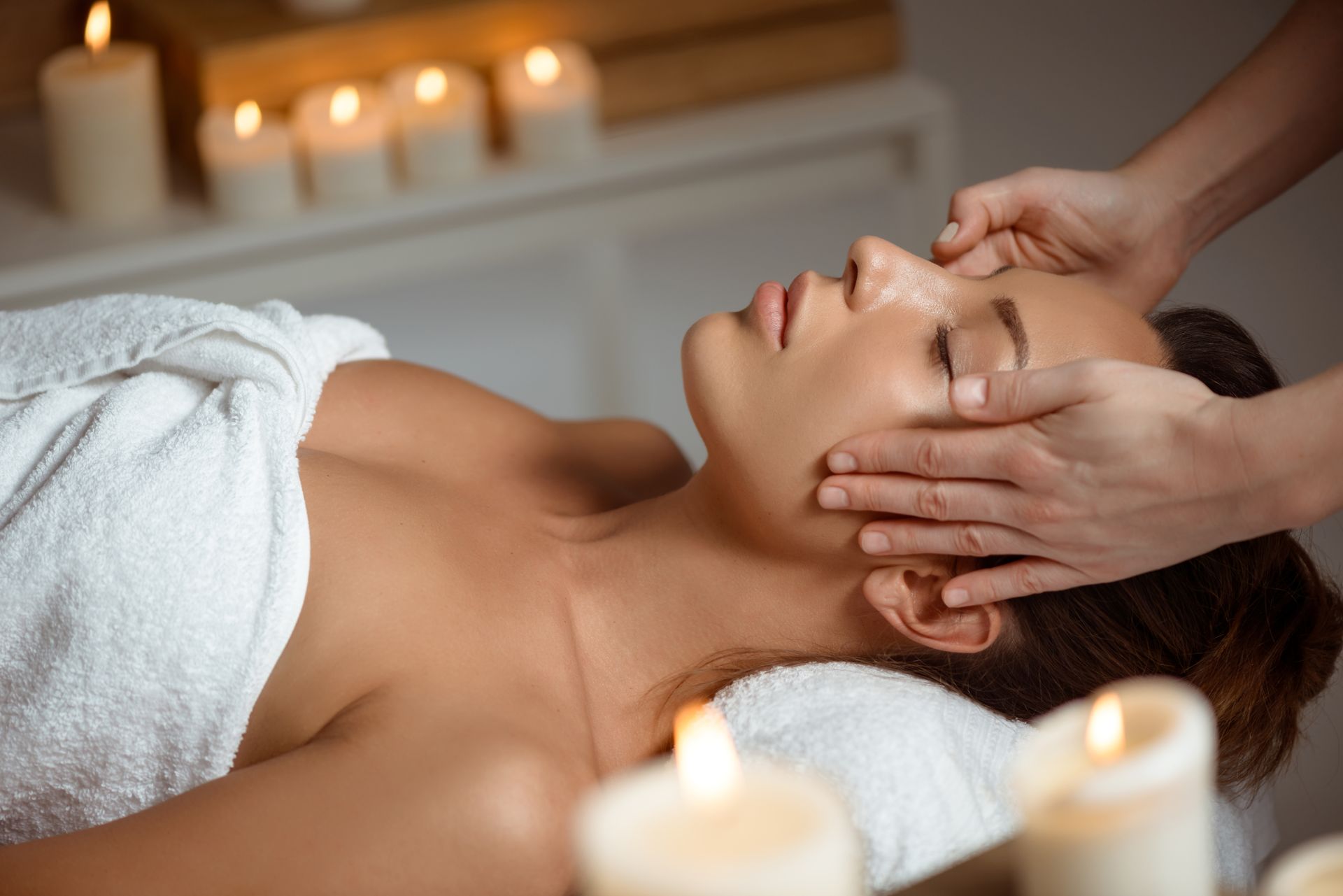 Eine Frau bekommt in einem Spa eine Kopfmassage, im Hintergrund leuchten Kerzen.