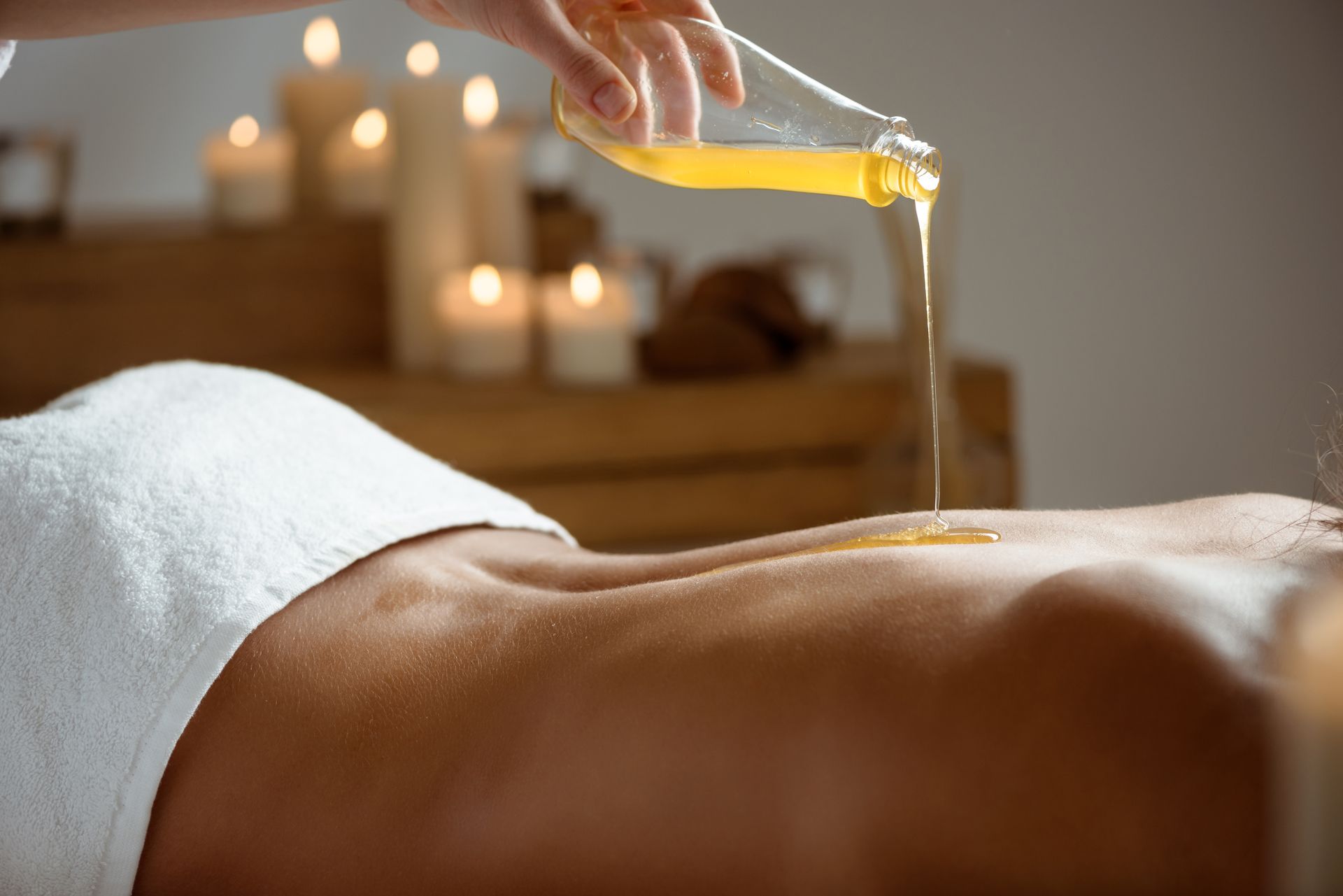 Eine Frau bekommt in einem Spa eine Massage, im Hintergrund leuchten Kerzen.
