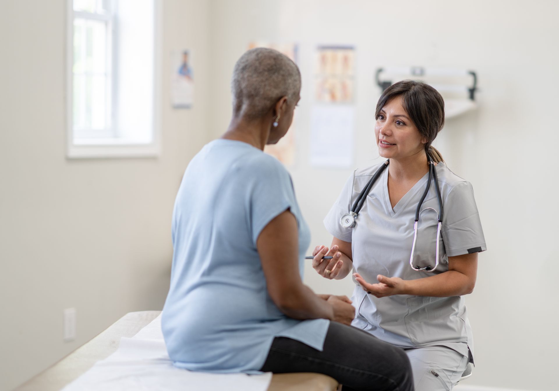 A nurse is talking to an older woman who is sitting on a bed.