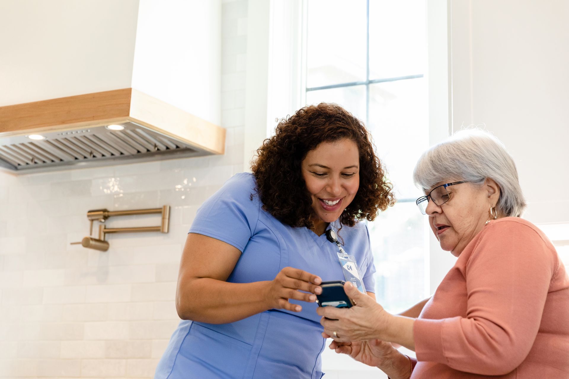 A nurse is teaching an elderly woman how to use a cell phone.