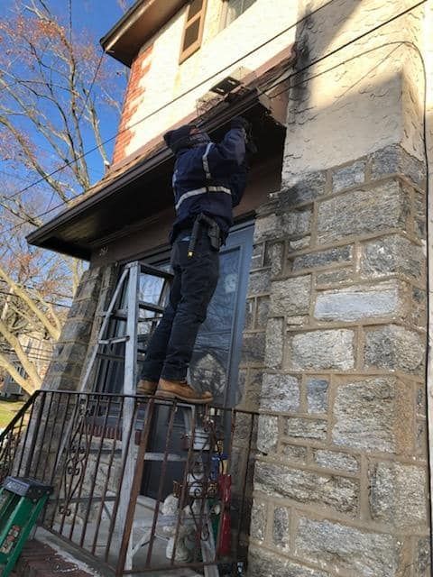 Person on ladder working on the roof of a stone building with a metal railing.