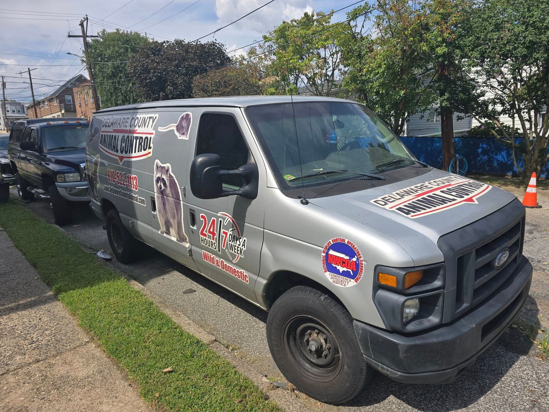 Gray van with company logo parked on a street; a black truck is parked behind it.