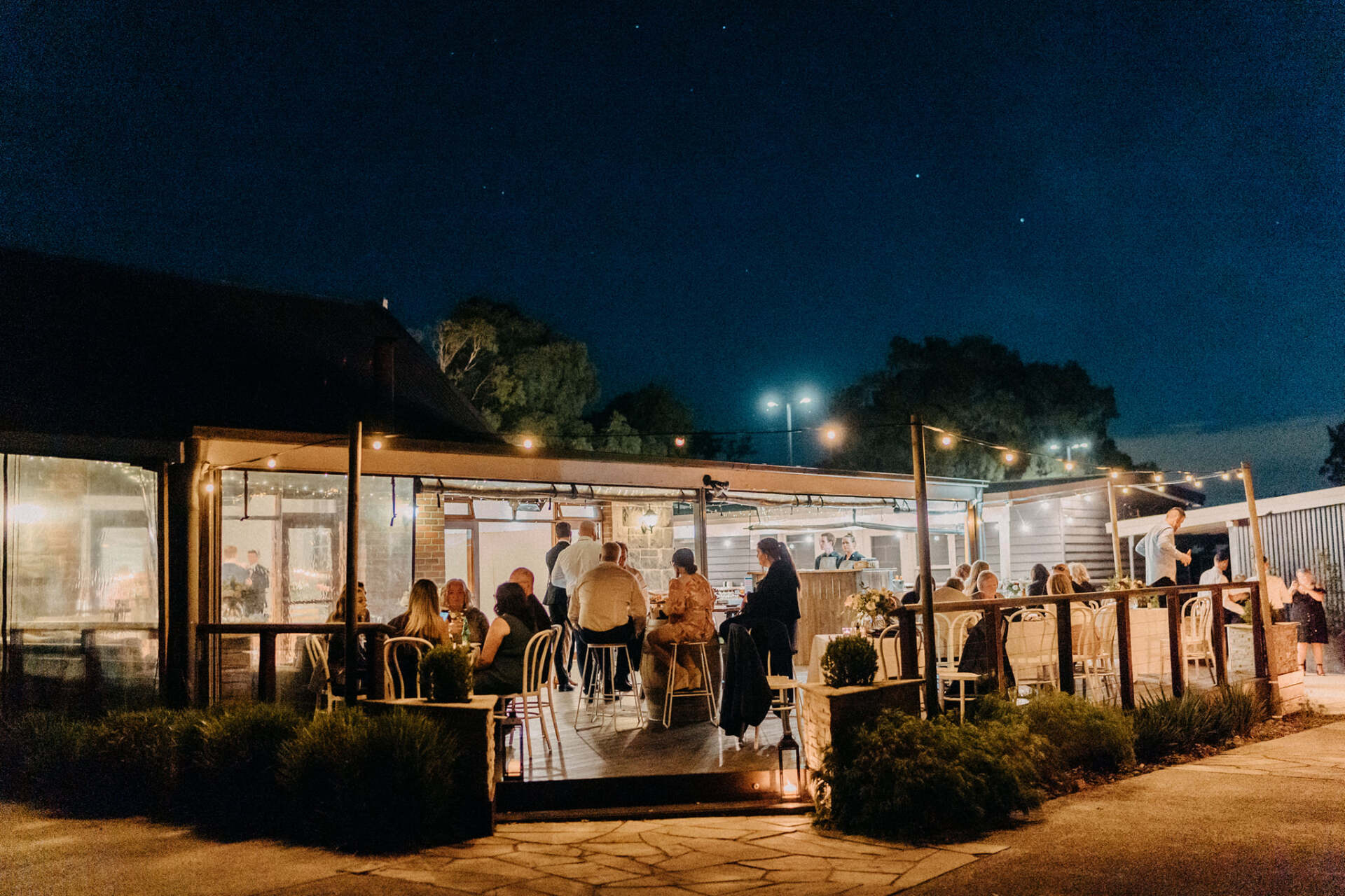 A group of people are sitting outside of a restaurant at night.