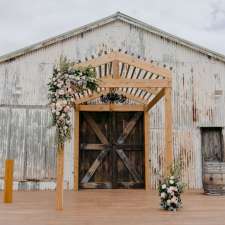 A white barn with a wooden arch and flowers in front of it.