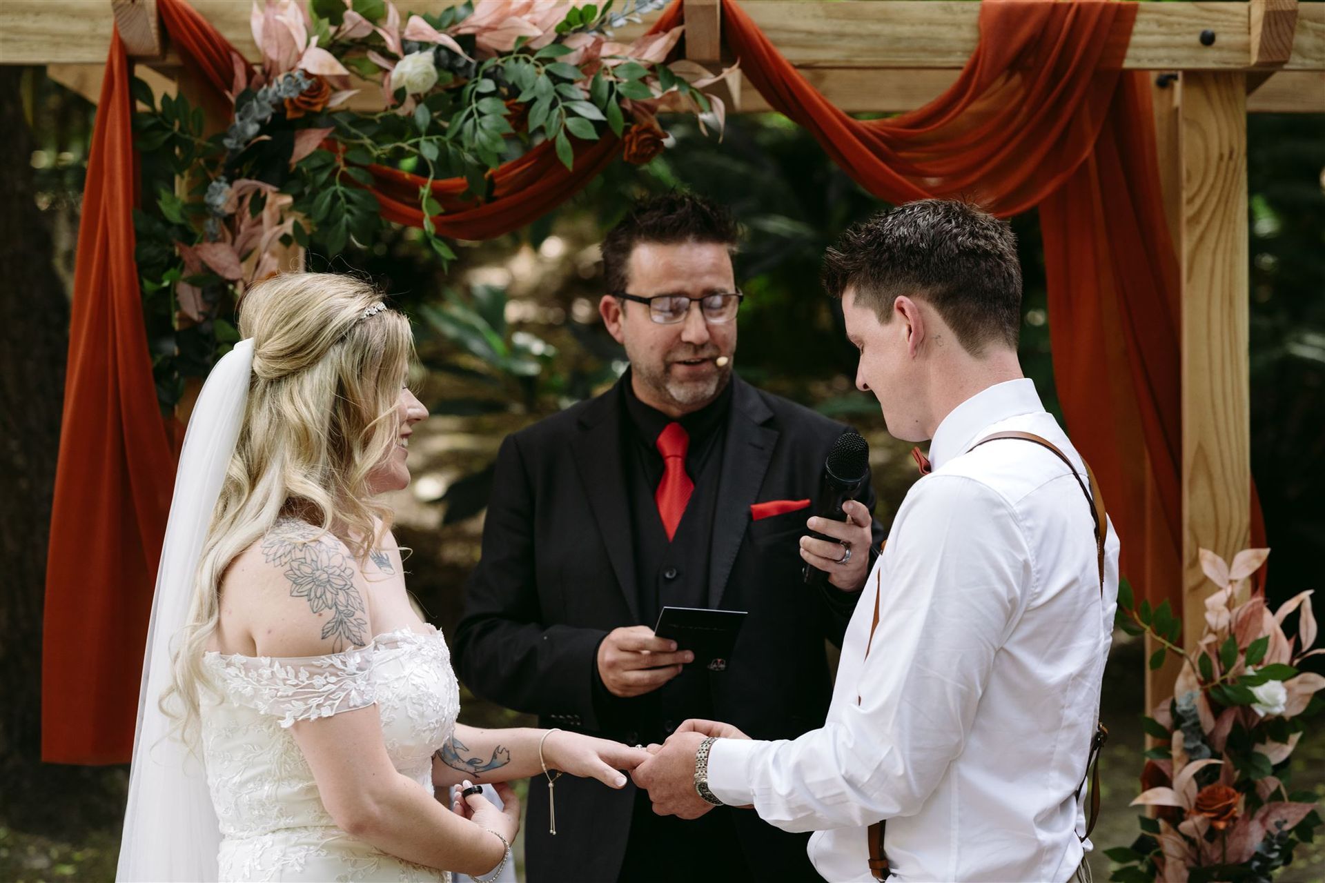 A bride and groom are getting married under a wooden arch.