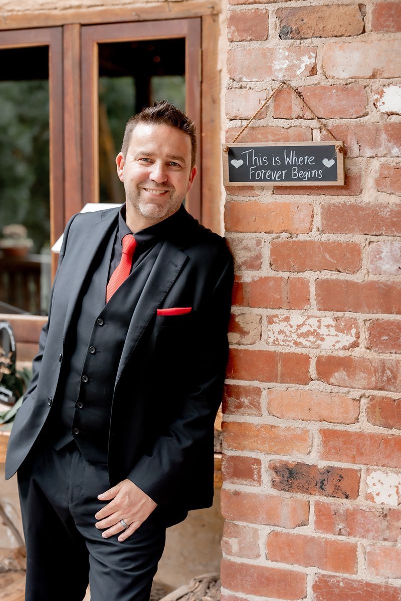 A man in a suit and tie is leaning against a brick wall. Jay Allen
