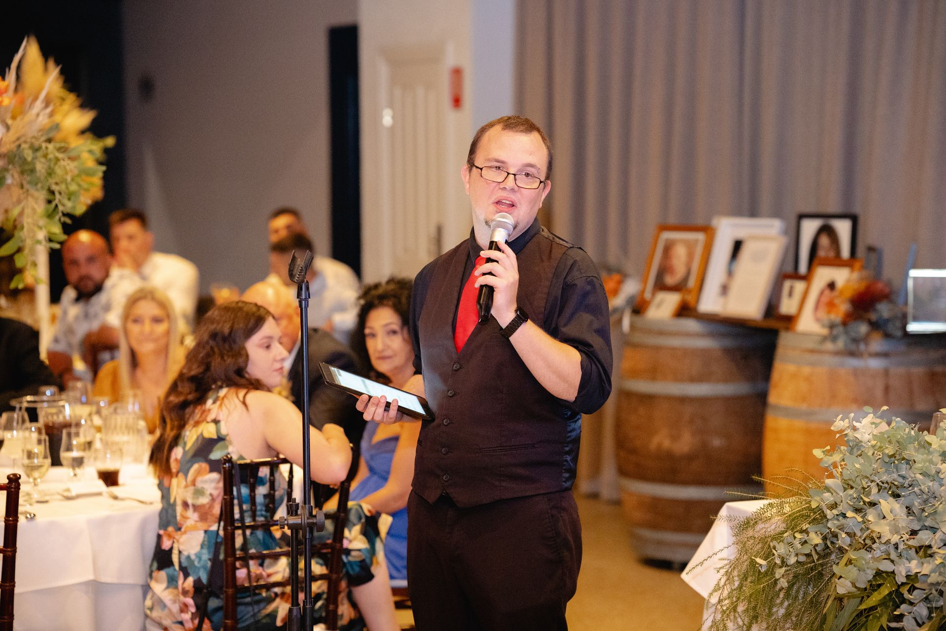 A man is standing in front of a microphone giving a speech at a wedding reception.