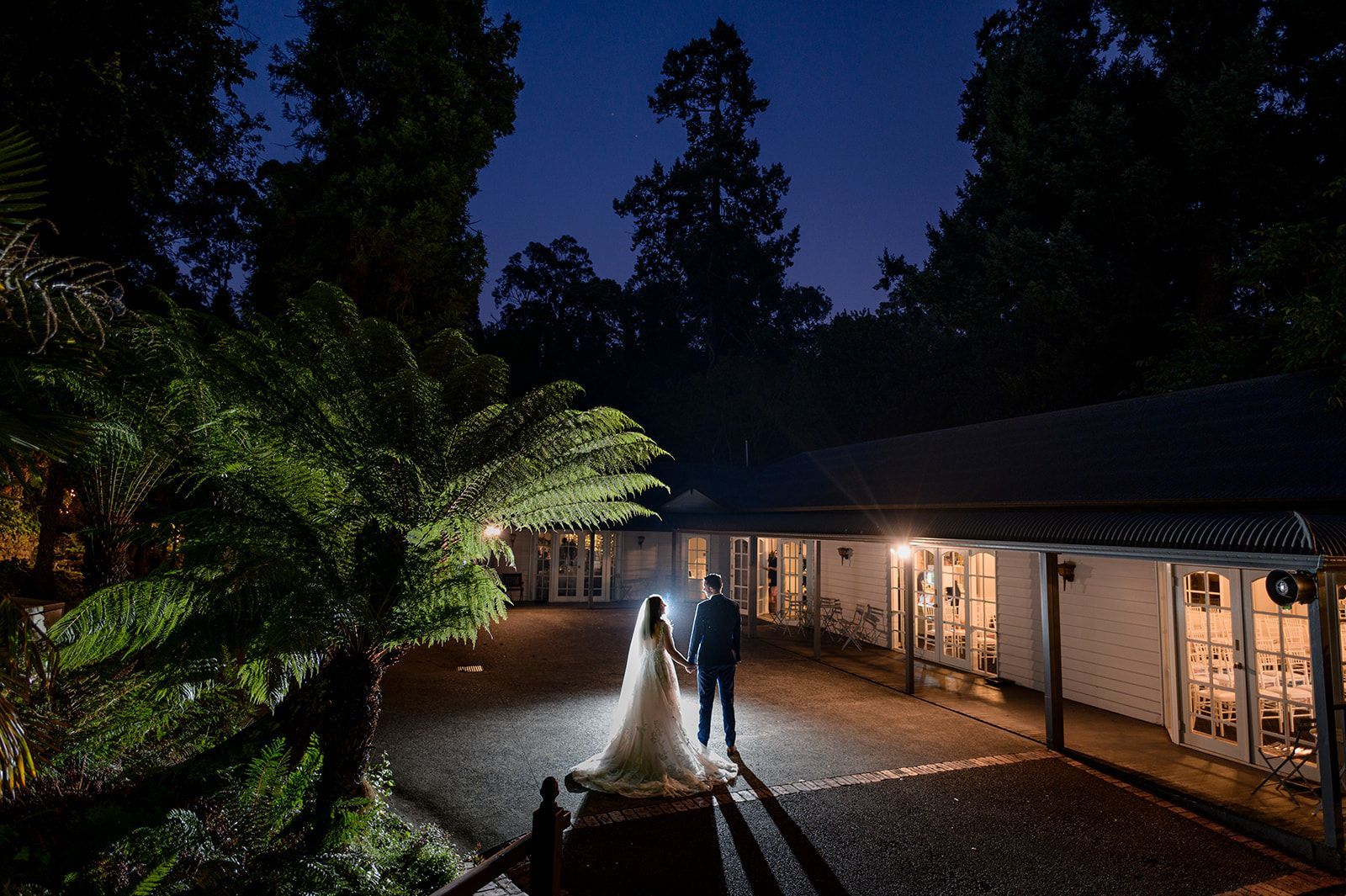 A bride and groom are standing in front of a building at night.