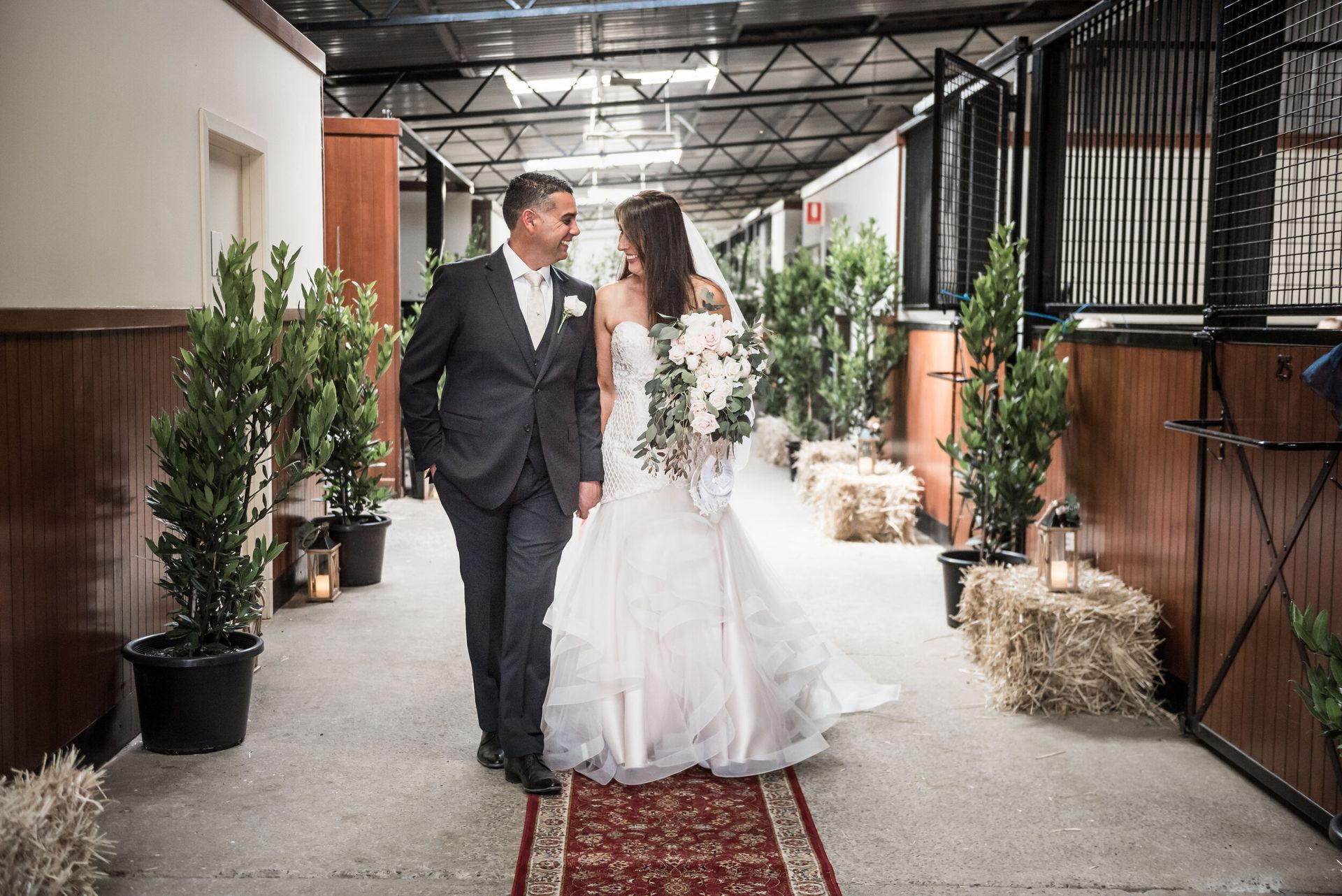 A bride and groom are walking down a hallway holding hands.