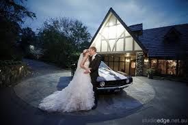 A bride and groom are kissing in front of a white car.