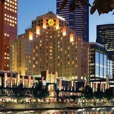 Hotel building lit up at dusk, with surrounding cityscape and water in the foreground.
