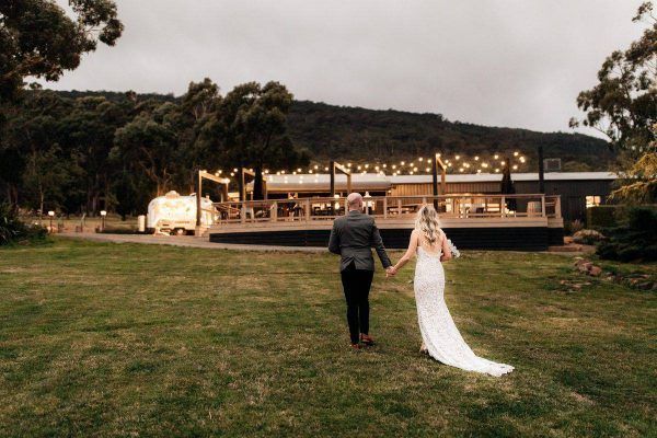 A bride and groom are walking in a field holding hands.
