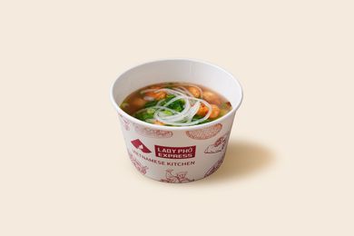 Paper cup of noodle soup with greens and shrimp on a light background