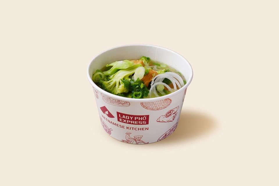 Paper cup of vegetable soup with broccoli and onion slices on a light background