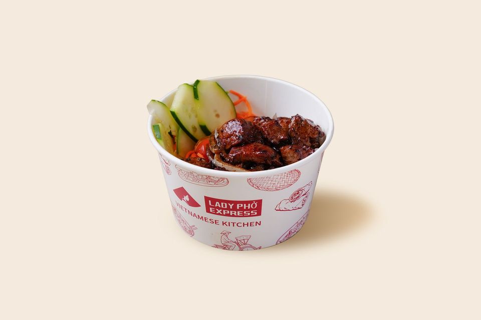 Takeout cup with glazed meat and sliced cucumber on a light background