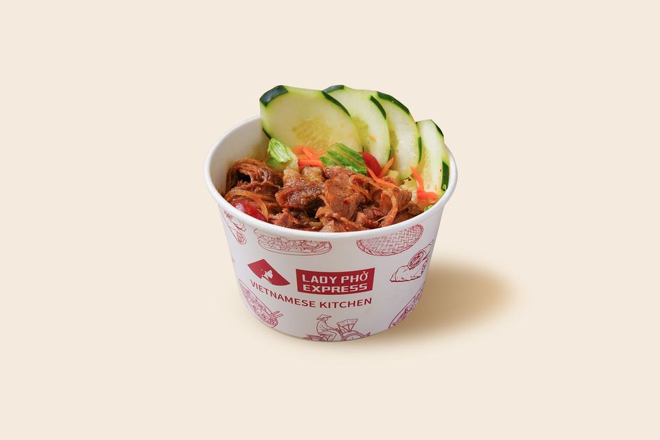 A takeout cup of shredded meat topped with cucumber slices on a light background