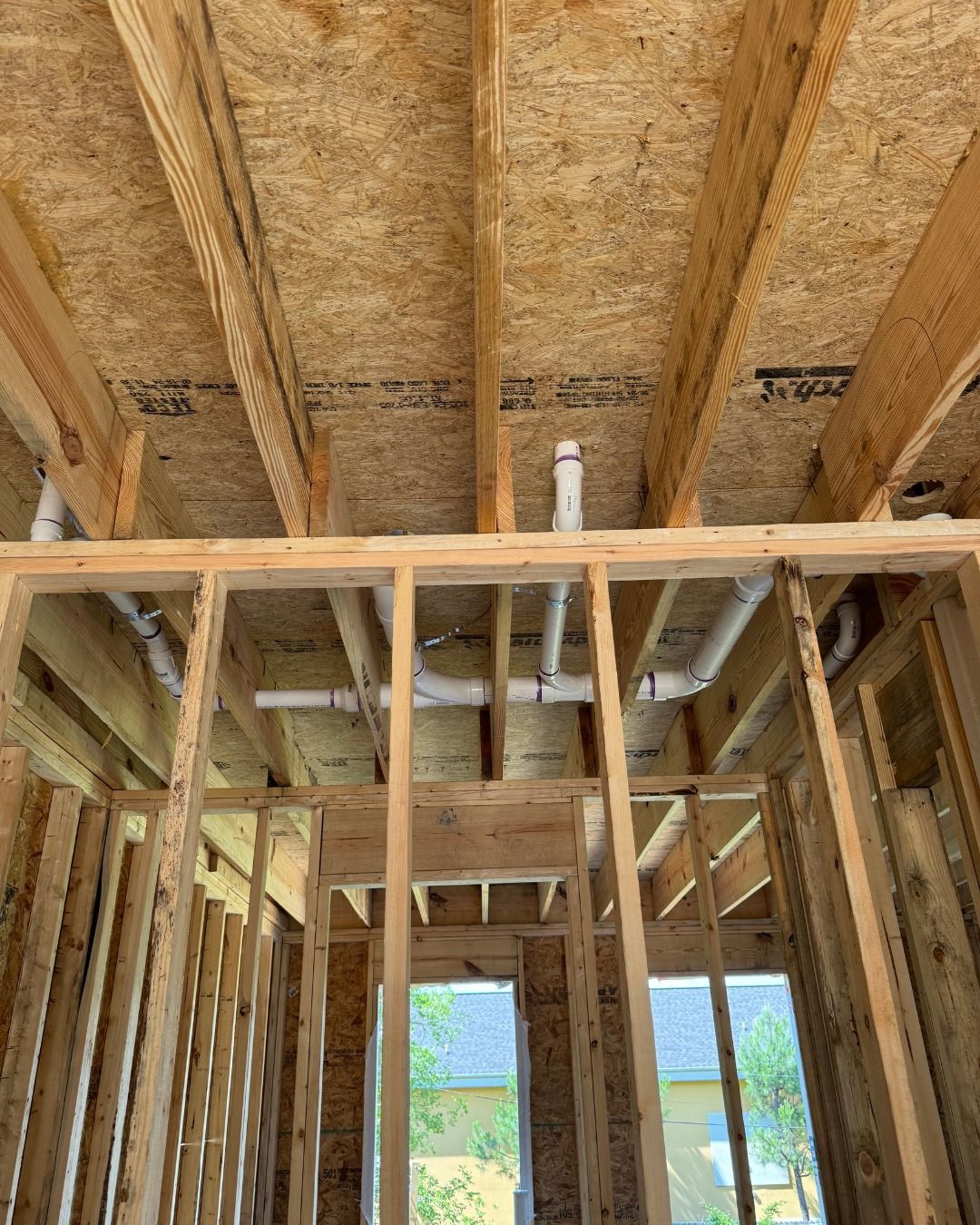 A house is being built with wooden beams and pipes coming out of the ceiling.
