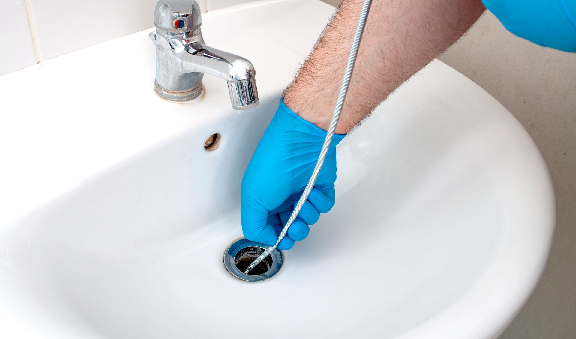 A person wearing blue gloves is cleaning a sink with a hose.