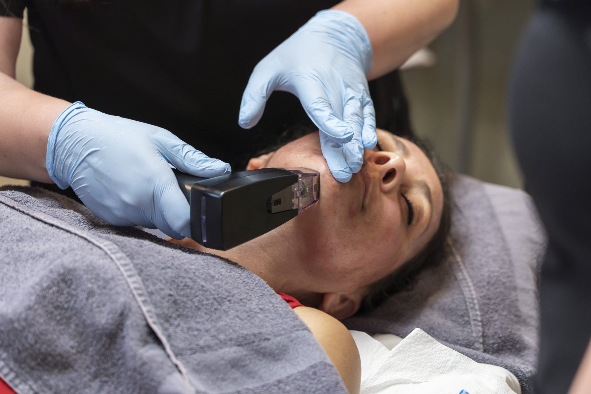 A woman is laying on a bed getting a treatment on her face.