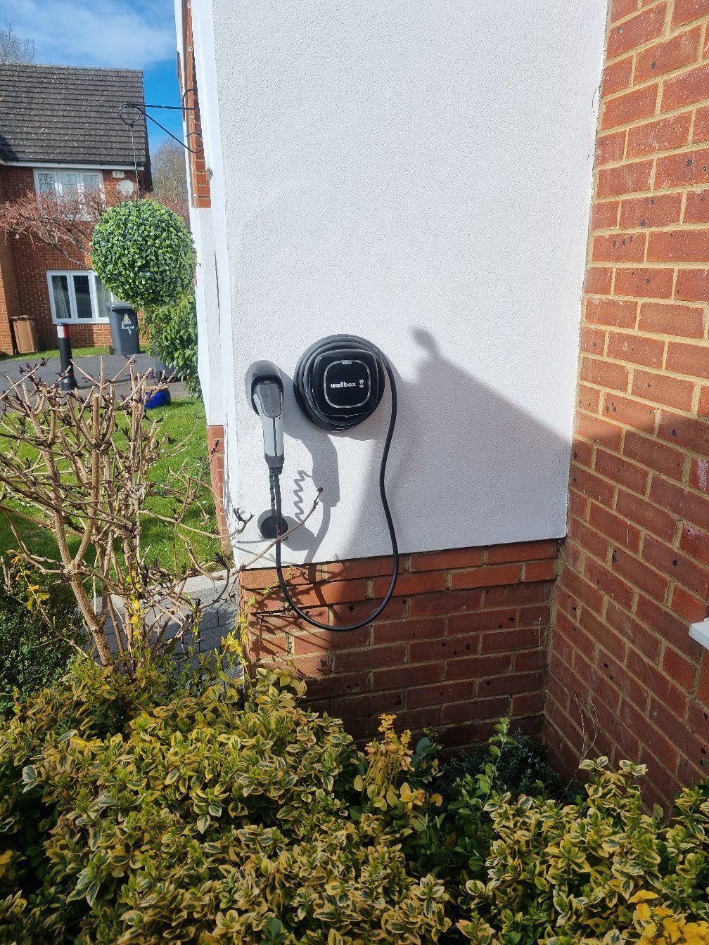 A car charger is attached to the side of a brick building.