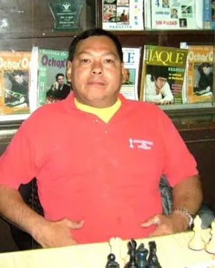 A man in a red shirt is sitting at a table with chess pieces