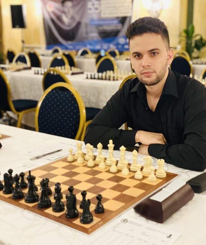 A man sits at a table with a chess board in front of him