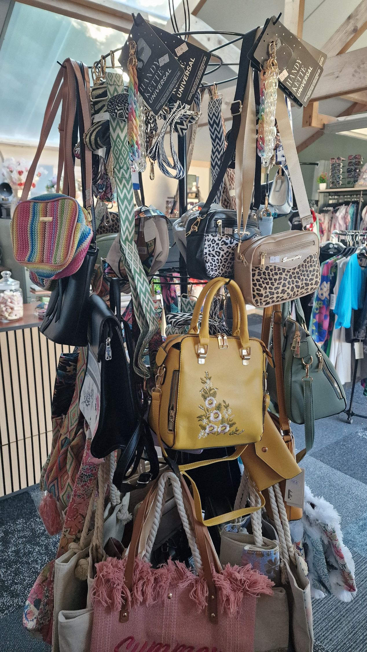 Kleurrijke handtassen hangen aan een kraam op een straatmarkt, waaronder een opvallende gele tas in het midden.
