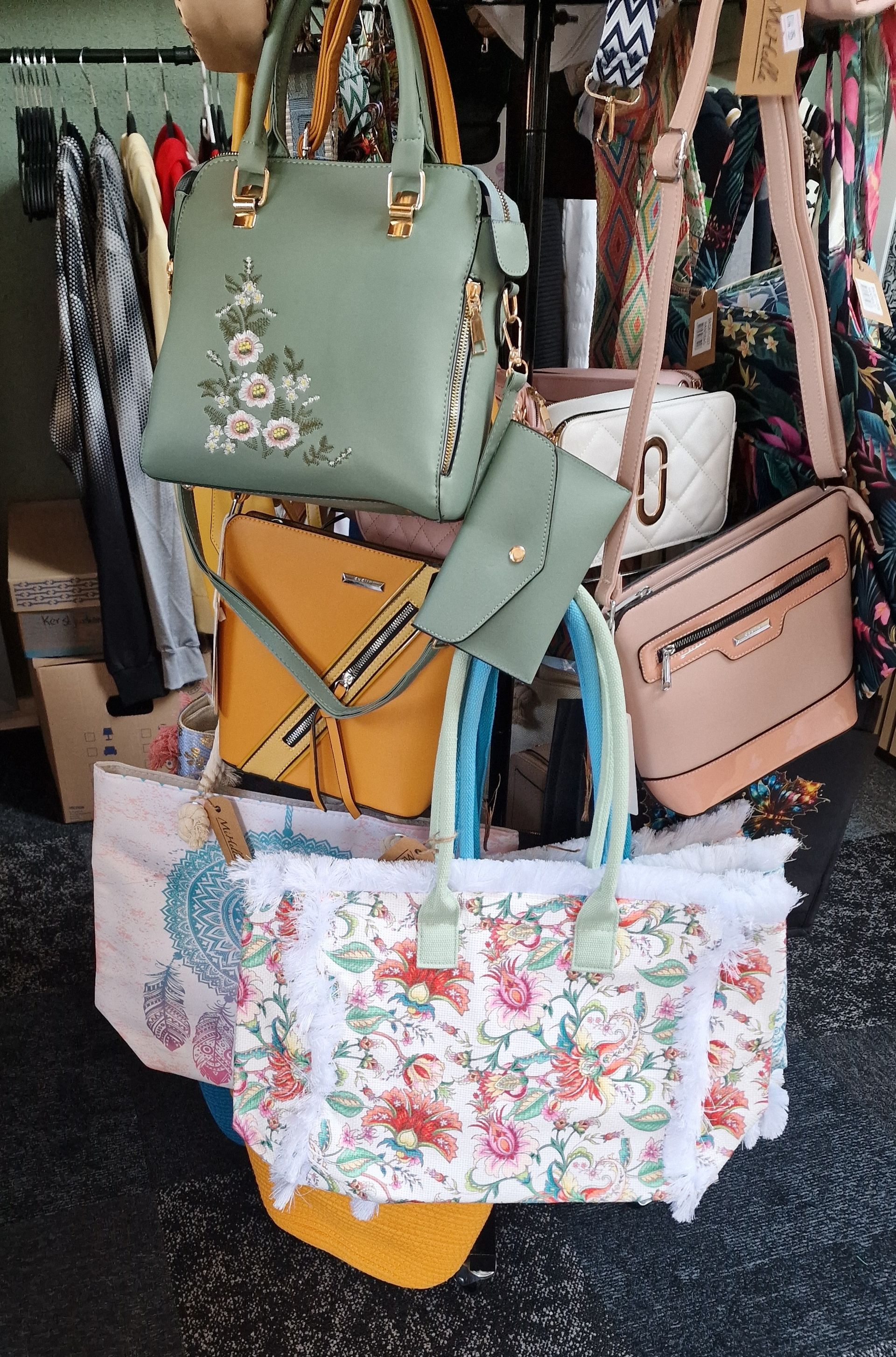 Kleurrijke handtassen hangen aan een displayrek, waaronder mintgroene, roze en tassen met bloemenprint.