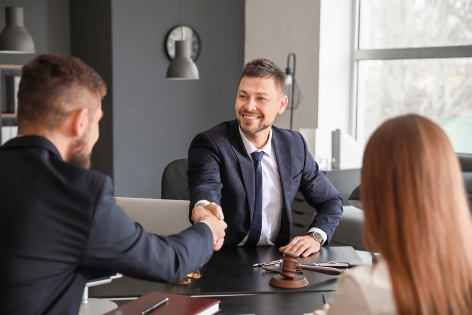 Lawyer shakes hands with client at a table in an office setting.