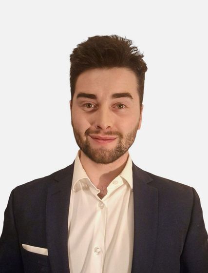 A man with a beard is wearing a suit and a white shirt.